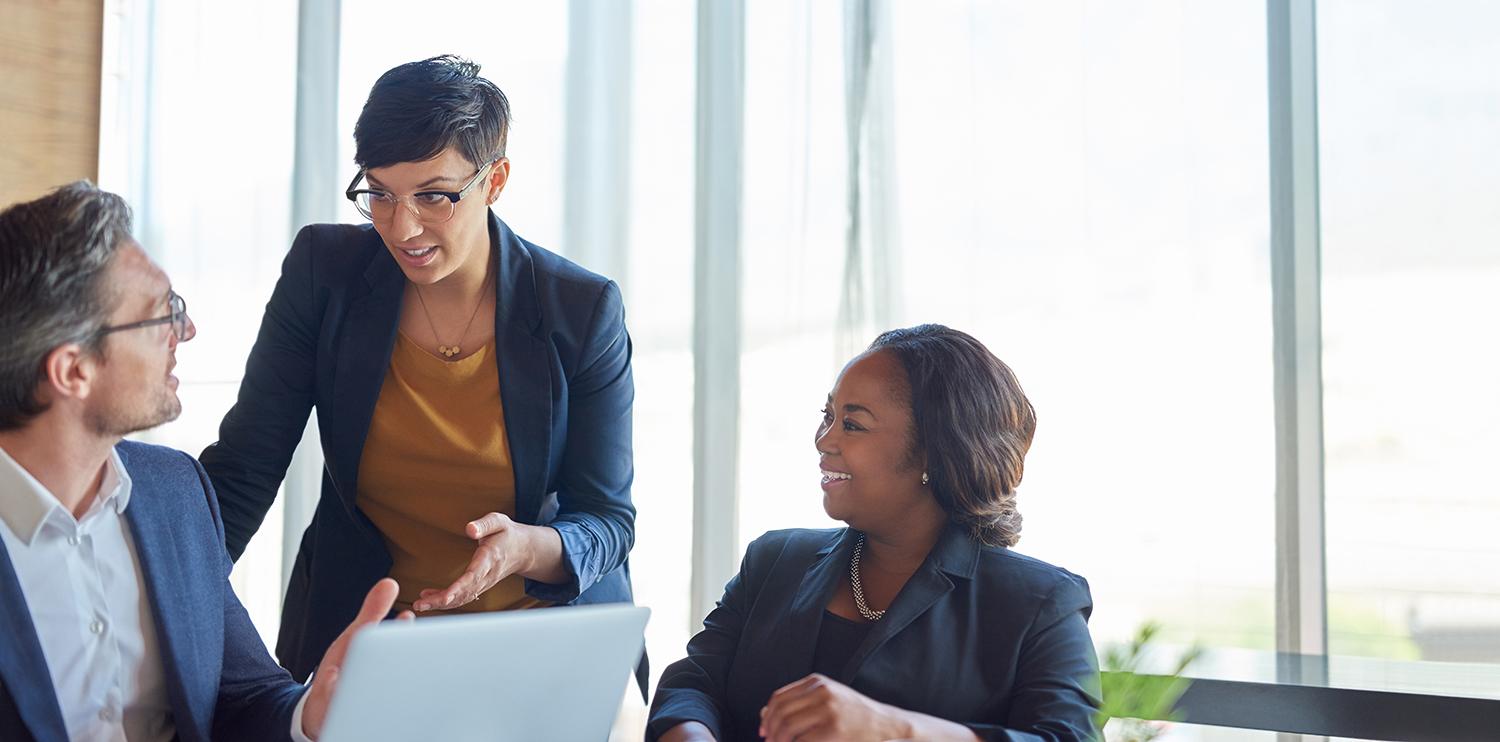 two female and one male colleague speak at a desk